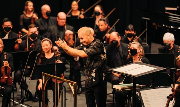 Yannick Nézet-Séguin standing in front of an orchestra on stage clapping towards the audience