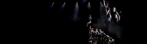 Acrobats form human columns on a spotlit stage, with two other dances in aboriginal clothes superimposed top-right