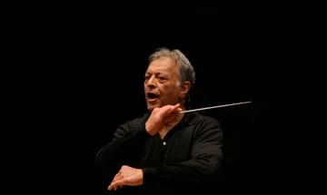 The conductor shown mid-performance, holding his baton on a darkly lit stage