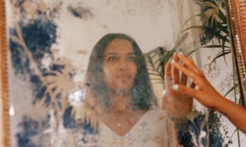 Dressed in a white dress with straight hair, the singer touches her reflection in a smudged, ornate mirror.