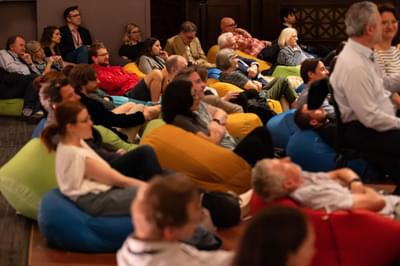 Audience members sit in colourful beanbags amongst orchestra members, smiling and listening