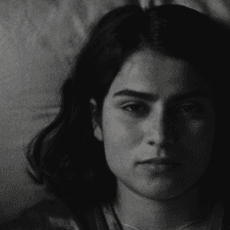 Anaita Wali Zada (Donya) lies on bed in black and white still from Fremont.