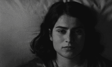 Anaita Wali Zada (Donya) lies on bed in black and white still from Fremont.
