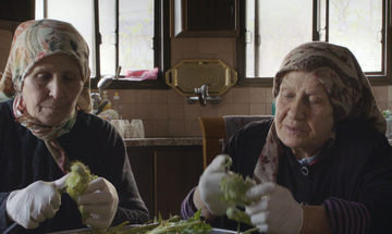 Two women sit at table chopping.