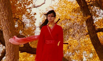 Woman wearing historical red costume holds sword against Autumnal backdrop.
