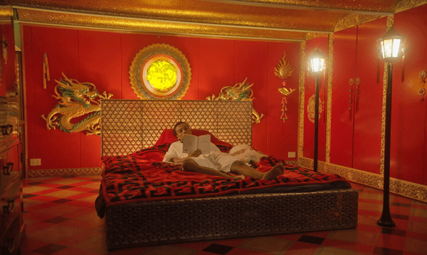Person lies on a bed reading, in a luxurious, red room