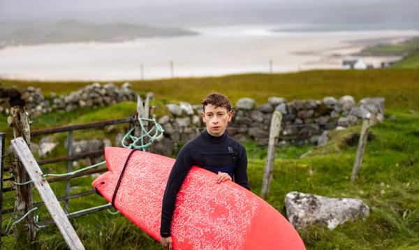 Louis McCartney (Dondo) holds a red surfboard in Silent Roar