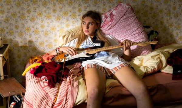 Ella Lily Hyland (Sas) sits on bed holding guitar in Silent Roar