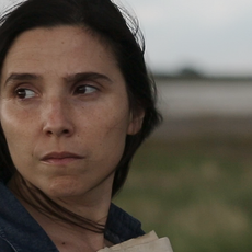 Laura Paredes stands in a field clutching papers to her chest.