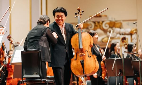 A Korean cello soloist smiles in gratitude and holds his cello up
