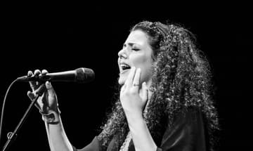 A black-and-white portrait of the singer giving an emotive performance onstage, holding the microphone in one hand and gesturing with the other.