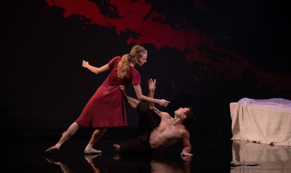 Two dancers mid flight. The woman is wearing a red dress and she stand over the top of the man