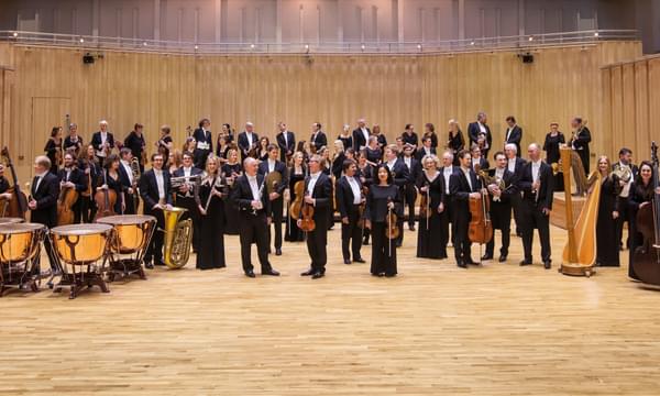 All of the members of the RSNO stand on a stage wearing formal dress with their instruments