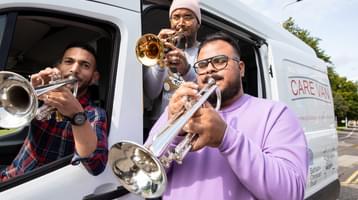 Three musicians blow trumpets out of the Bethany Christian Trust Care Van