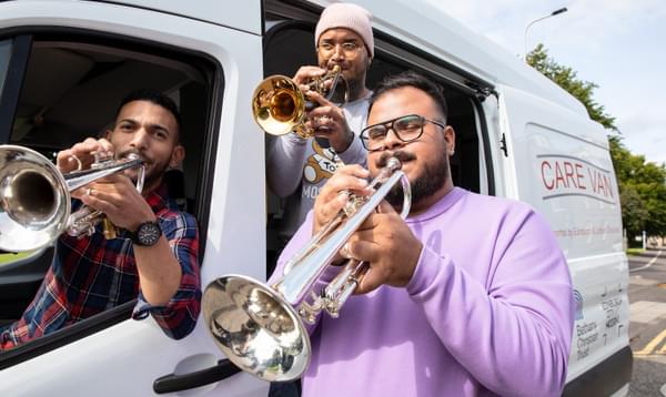 Three musicians blow trumpets out of the Bethany Christian Trust Care Van