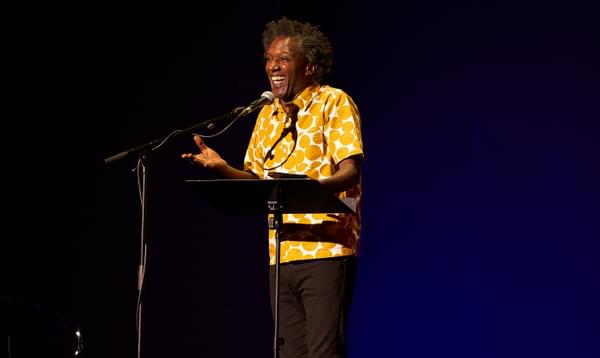 A man in a yellow patterned shirt smiles while standing behind a microphone