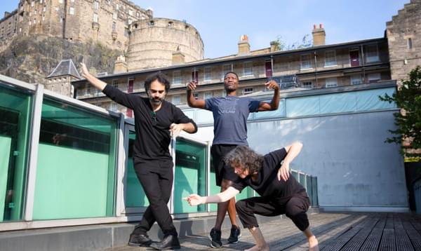 Three people pose in dancing positions in front of Edinburgh castle