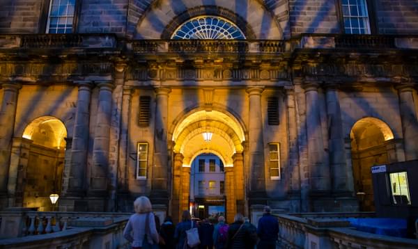 Lights shine across a grand archway of the Edinburgh University college quad as people walk through