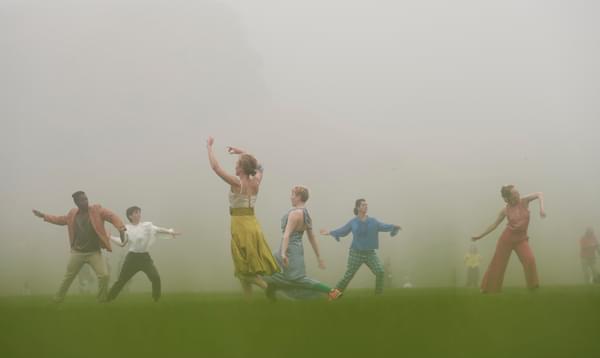 A group of people dance in colourful clothing, surrounded by mist
