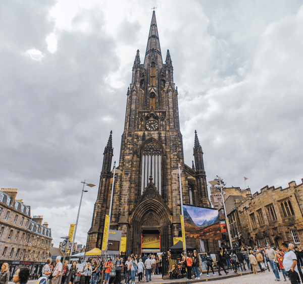 The front of The Hub, a neo-gothic church at the top of the Royal Mile, with many people walking in front of it