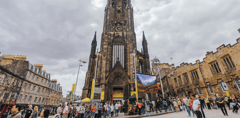 The front of The Hub, a neo-gothic church at the top of the Royal Mile, with many people walking in front of it