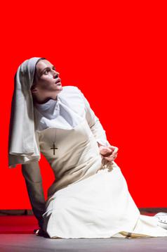A woman in a white nun's habit sits against a red background leaning against her left arm