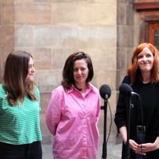 Three women stand in front of a microphone in the vestibule of Leith Theatre