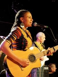 Sona Jobarteh pictured performing onstage, playing guitar and singing into a microphone.