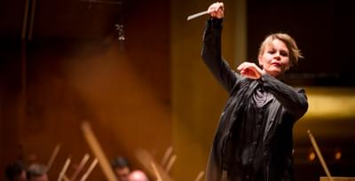 The conductor pictured mid-movement, with her arms raised and the baton held high above her head.