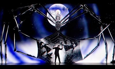 A man stands caught in a spider's web surrounded by a giant spider