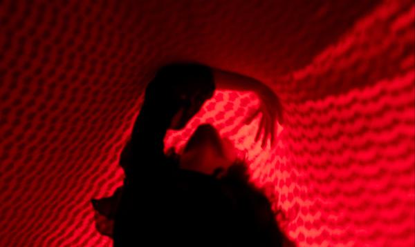 A woman reaches to the ceiling, surrounded in a vibrant red cloth