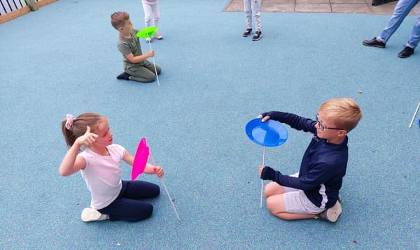Children sit on the floor and practice spinning colourful plates on sticks