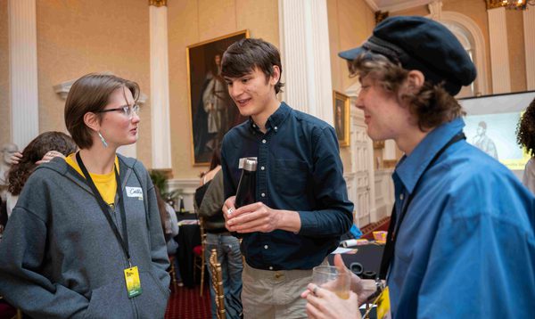Three teenagers stand in a group, talking.