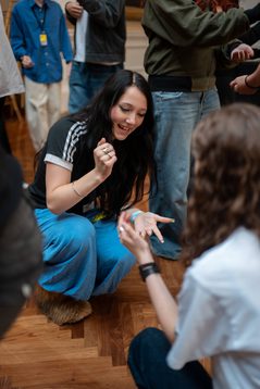 A teenager crouches on the floor playing rock-paper-scissors with another teen.