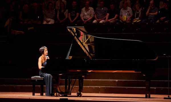 A woman with short dark hair plays piano in a dark blue dress