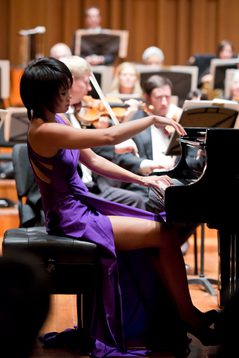 A woman in a purple dress leans back as she plays piano